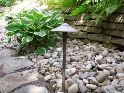 An outdoor light fixture in a stone garden with a green plant next to it
